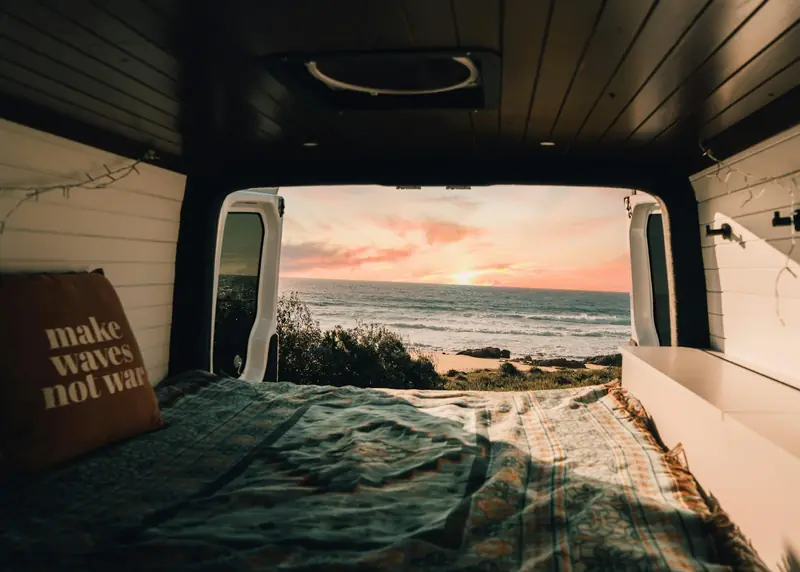 View from a campervan bed through the open rear doors to the sea at sunrise